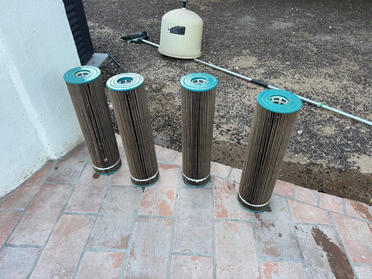Four cylindrical pool filter cartridges with dark, loaded pleats standing on a patio before Runestone filter cleaning