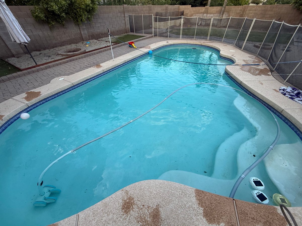 Aerial view of a residential swimming pool with bright turquoise water, spa tub, and safety fence enclosure