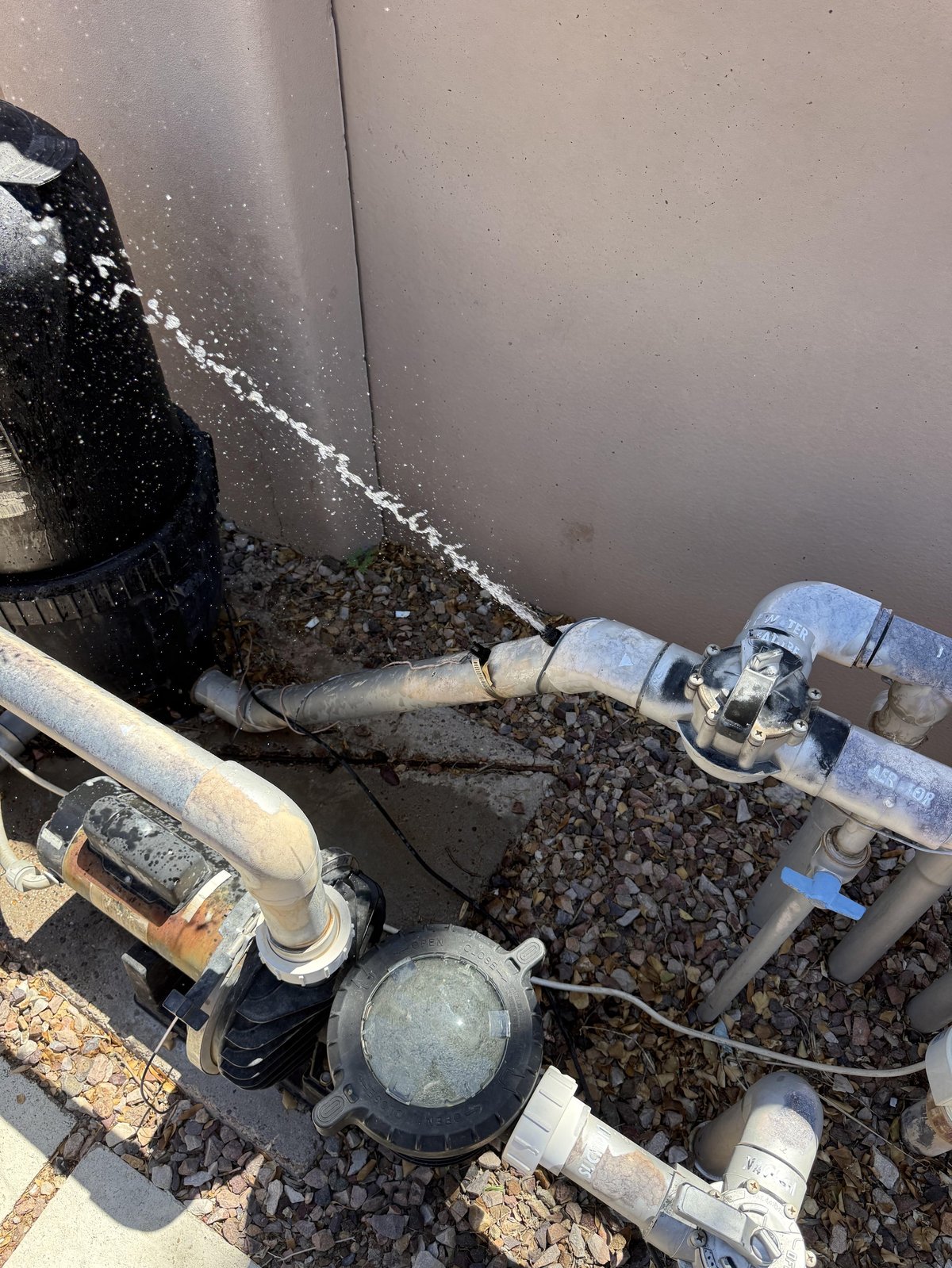 Exterior plumbing and valve system with pipes, connectors, and pumps mounted against a concrete wall