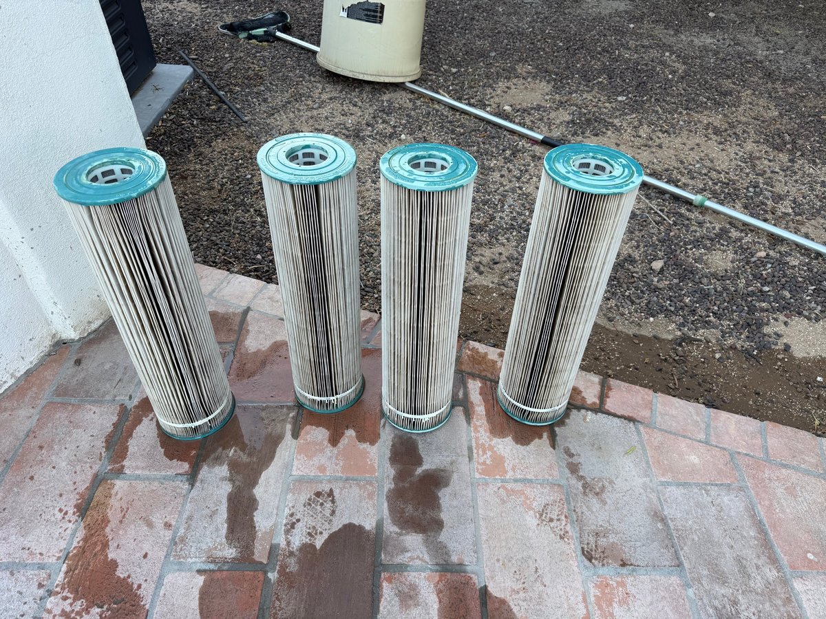 The same four pool filter cartridges cleaned to a pale, uniform pleat on a freshly washed patio after Runestone filter service
