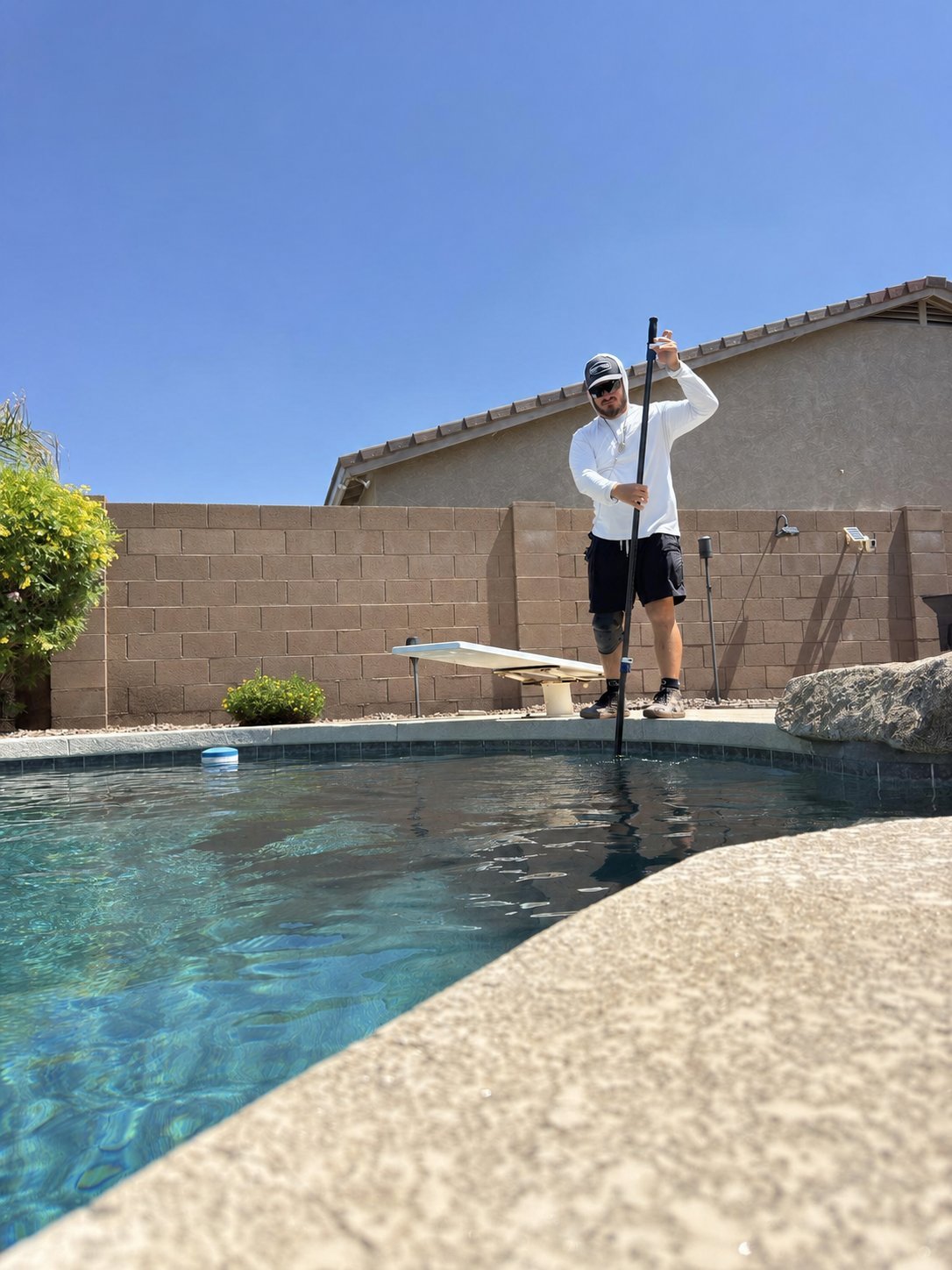 Man in white shirt stand-up paddleboarding on backyard pool on sunny day